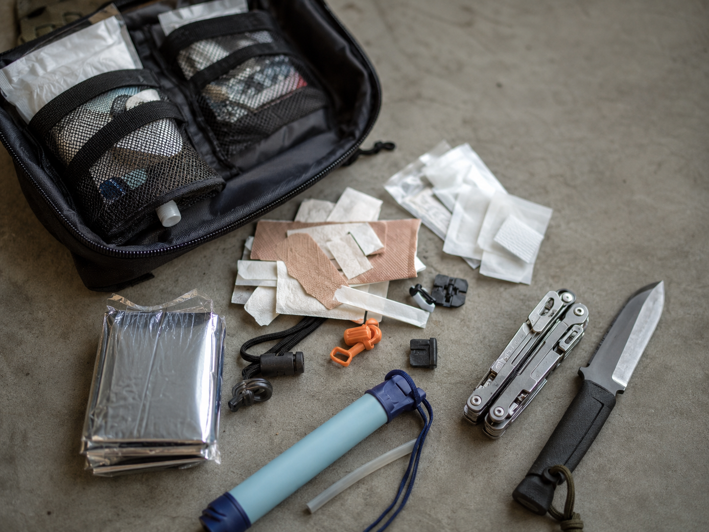 Open survival kit spread showing many small items and a few useful tools